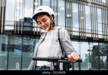 Giovane donna in casco che tiene un manubrio di scooter elettrico in città Foto Stock
