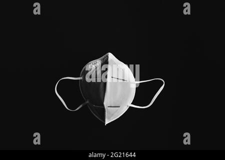 Foto in bianco e nero del lato anteriore della maschera KN95 isolata in nero Foto Stock