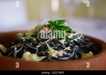 Spaghetti al Nero di Seppia con pomodori ed erbe in un piatto di ceramica in una sala da pranzo pubblica, davanti e sullo sfondo Foto Stock