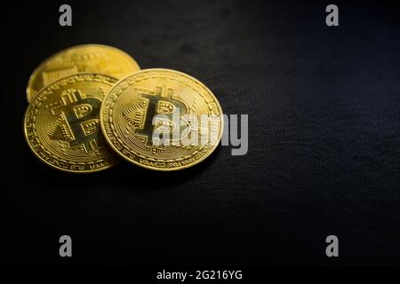 Primo piano di tre monete dorate di bitcoin su uno sfondo scuro con spazio di copia Foto Stock