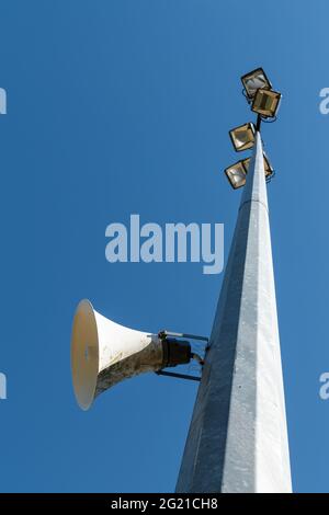 Vista ad angolo basso di una torre in un campo sportivo con altoparlante per la comunicazione al pubblico e proiettori contro il cielo blu chiaro Foto Stock