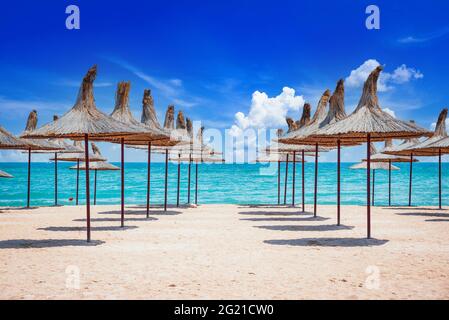 Mangalia, Romania. Spiaggia di sabbia del Mar Nero con ombrelloni di paglia su un cielo limpido e blu, soleggiata giornata estiva. Foto Stock