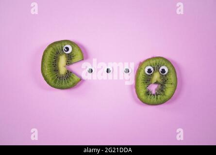 Fette di Kiwi con occhi giocattolo su sfondo rosa tenue alla moda. Scena di mangiare divertente e spaventosa. Idea di Halloween. Frutta tropicale e concetto estivo. Foto Stock