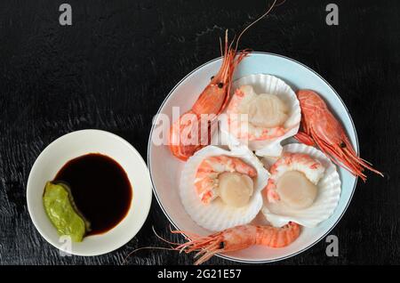 Capesante grezzo naturale con gamberi bolliti nel lavandino in una ciotola di ceramica con salsa di soia e wasabi su fondo scuro. Messa a fuoco selettiva. Foto Stock