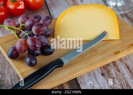 Primo piano di un coltello su un tagliere di legno con una fetta di formaggio accanto a un grumo di uva Foto Stock