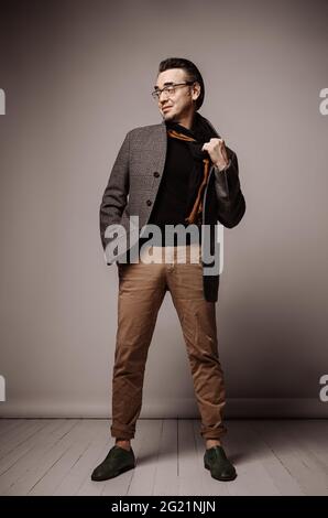 Hipster uomo adulto sorridente ottimista in pantaloni e giacche di plaid si stacca togliendo la sciarpa e guardandosi da parte Foto Stock