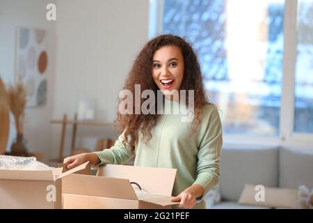 Felice giovane donna che disimballa il pacco a casa Foto Stock