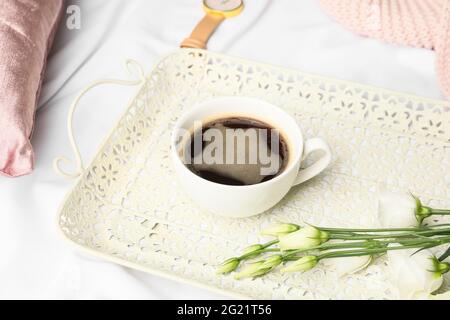 Vassoio con tazza di caffè e fiori sul letto Foto Stock