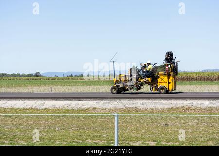 Una macchina per la marcatura di linee che segna le corsie su una nuova autostrada non aperta che passa attraverso i campi di canna da zucchero a Mackay, Queensland, Australia. Foto Stock