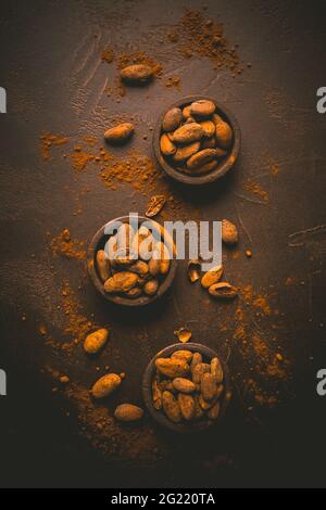 Fagioli di cacao organici in piccole ciotole su sfondo marrone. Cottura e cottura degli ingredienti Foto Stock