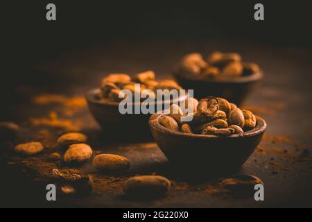 Fagioli di cacao organici in piccole ciotole su sfondo marrone. Cottura e cottura degli ingredienti Foto Stock