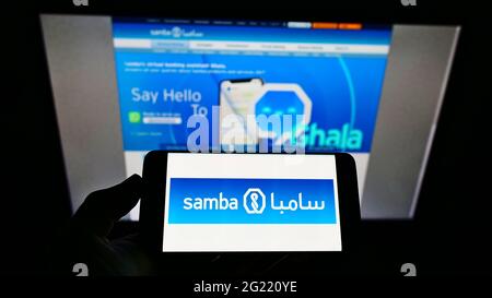 Persona in possesso di smartphone con logo della società Saudita Samba Financial Group SJSC sullo schermo davanti al sito Web. Mettere a fuoco il display del telefono. Foto Stock