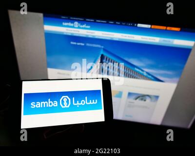 Persona in possesso di smartphone con logo della società Saudita Samba Financial Group SJSC sullo schermo davanti al sito Web. Mettere a fuoco il display del telefono. Foto Stock