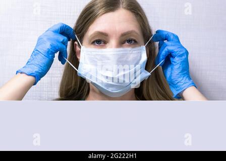 ragazza mette su una maschera medica, tiene i suoi guanti, dispositivi di protezione personale contro i virus Foto Stock