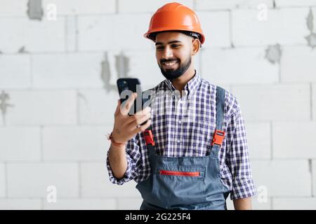 Costruttore indiano che controlla un messaggio sul suo telefono cellulare o che fa una chiamata in una nuova casa di costruzione Foto Stock