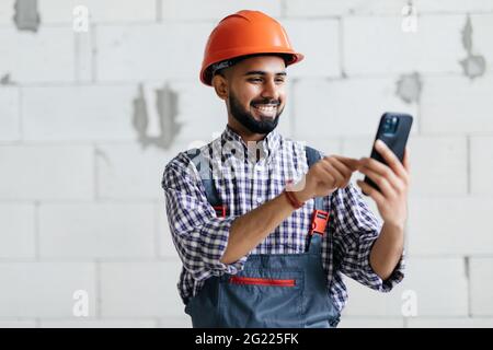 Costruttore indiano che controlla un messaggio sul suo telefono cellulare o che fa una chiamata in una nuova casa di costruzione Foto Stock