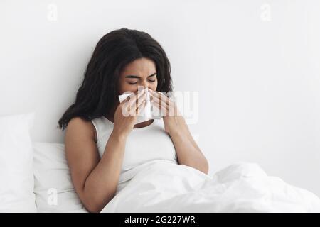 Influenza. Malata africana americana donna soffia naso che cola starnuti, seduto a letto, copia spazio Foto Stock