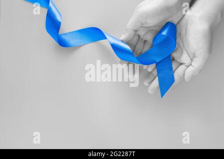 Mani che tengono il nastro blu profondo su sfondo blu con spazio per la copia. Cancro colorettale consapevolezza cancro del colon di persona anziana e mondo diabete giorno Chi Foto Stock