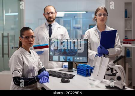 Team di scienziati in laboratorio che guardano la telecamera in un laboratorio moderno attrezzato. Gruppo di medici che esaminano l'evoluzione del virus utilizzando l'alta tecnologia per la ricerca scientifica, sviluppo di vaccini. Foto Stock