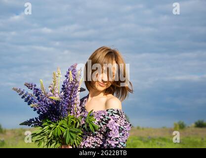 La faccia della donna felice coperta di capelli contro il cielo blu. Nelle mani di un bouquet di fiori selvatici. Foto d'atmosfera, stagione fiorente, giornata spensierata Foto Stock