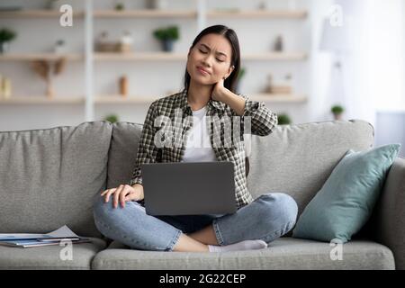 Sconvolto donna asiatica che soffre di dolore al collo durante l'uso del computer portatile Foto Stock