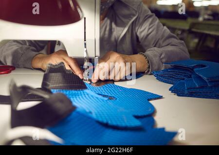 Lavoratrice femminile presso la fabbrica di scarpe che fa dettagli sneaker su macchina da cucire industriale Foto Stock