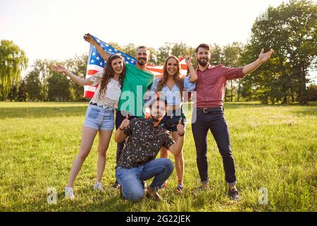 Gruppo di amici con bandiera americana celebrano la giornata di indipendenza americana in piedi nel parco. Foto Stock