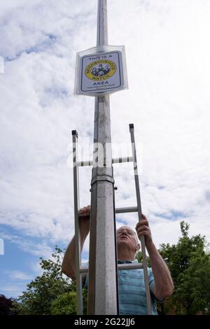 Un anziano locale discende la sua scala dopo aver fissato in posizione, un cartello di vigilanza di quartiere su un palo di lampada, il 30 maggio 2021, a Nailsea, Somerset del Nord, Inghilterra. Foto Stock