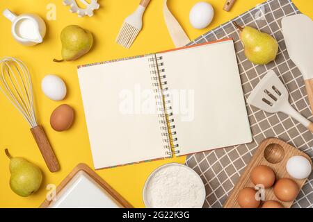 Aprire il taccuino bianco, gli ingredienti da forno e l'utensile da cucina, sullo sfondo giallo. Modello per cucinare ricette o il vostro disegno. Vista dall'alto piatto Mocku Foto Stock