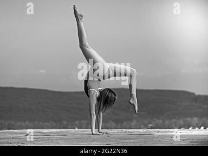 Bella donna atletica si allunga e fa un ponte sullo sfondo del cielo. Foto Stock