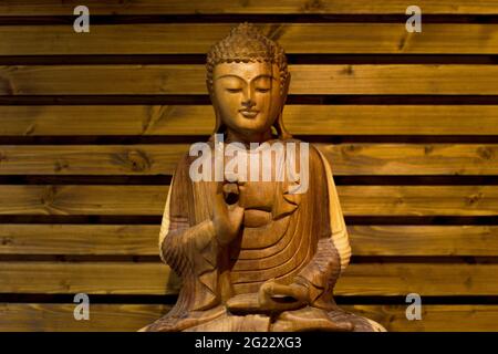 c'è un buddha illuminato in legno che medita su uno sfondo di legno Foto Stock
