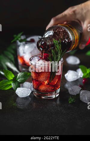 Cocktail liquore, vodka, ghiaccio e rosmarino. Bevanda fresca rinfrescante, liquore di frutti di bosco o cocktail alcolico rosso. Messa a fuoco selettiva Foto Stock