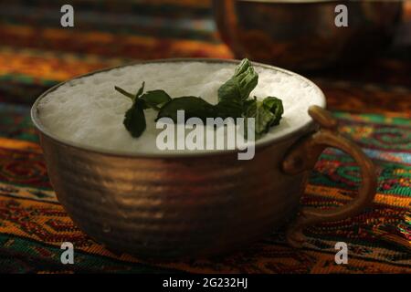 Bevanda sana e naturale ayran servita in tradizionale tazza di rame Anatolia fatta a mano decorata con foglie di menta fresca. Foto Stock