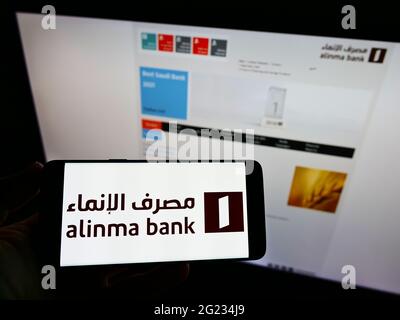 Persona in possesso di smartphone con logo della società finanziaria Saudita Alinma Bank sullo schermo davanti al sito Web. Mettere a fuoco il display del telefono. Foto Stock