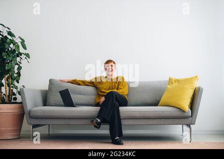 donna d'affari seduta sul divano e sorridente. Donna sicura di sé con un computer portatile seduto sul divano nella hall dell'ufficio. Foto Stock
