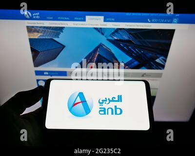 Persona che tiene il cellulare con il logo della società finanziaria Saudita Arab National Bank sullo schermo di fronte alla pagina web. Mettere a fuoco il display del telefono. Foto Stock