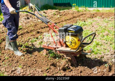 arando la terra nel giardino con un lavoro agricolo di cultivator. su arando il campo per semina semi. un uomo aratura la terra usando motocoltivatore Foto Stock