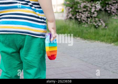 Un bambino piccolo tiene un giocattolo anti-stress pop con un posto per il testo sullo sfondo del parco della città. Foto Stock