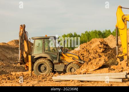 Escavatore giallo durante i lavori di terra in cantiere. Retroescavatore scavare il terreno per la fondazione e per la posa tubi fognari teleriscaldamento. EH Foto Stock