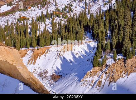 In una valle montana nella stagione invernale, sono state gettate delle ombre dalla forma interessante di un certo numero di abeti sulla neve; diverse case in legno nel backgro Foto Stock