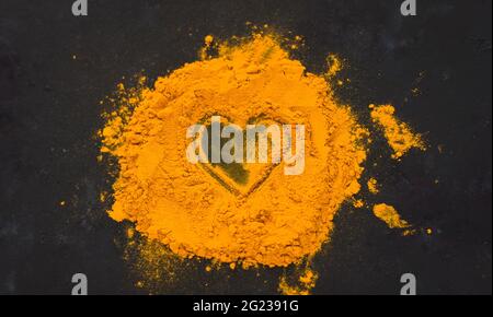 Spezie dell'India curcuma spezie sparse su uno sfondo scuro a forma di cuore, cibo sano Foto Stock