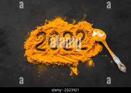 Le spezie dell'India curcuma è sparso su uno sfondo scuro nella forma del nuovo anno 2022 Foto Stock