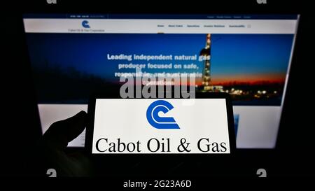 Persona che tiene il cellpohone con il logo della società americana Cabot Oil and gas Corporation sullo schermo di fronte alla pagina web aziendale. Mettere a fuoco il display del telefono. Foto Stock