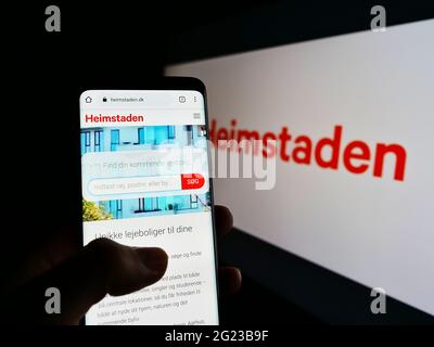 Persona che detiene il logo del sito web del telefono cellulare della società immobiliare svedese Heimstaden AB sullo schermo davanti al logo. Mettere a fuoco il centro del display del telefono. Foto Stock