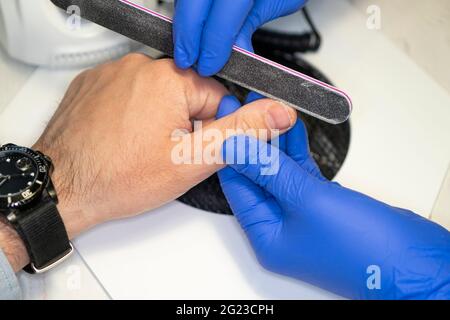 una mano dell'uomo sulla procedura di manicure. Manicurista che lime le unghie dell'uomo in salone. Manicure uomo. Cura delle mani per gli uomini Foto Stock