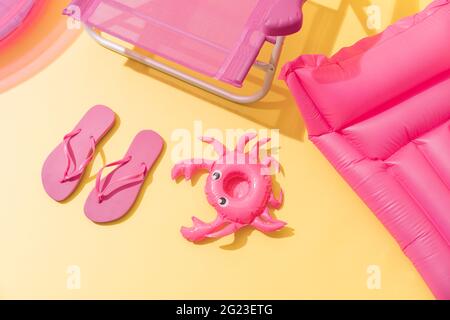 Una sedia da spiaggia rosa con infradito rosa, un tappetino gonfiabile rosa e un granchio gonfiabile rosa. Vista dall'alto Foto Stock