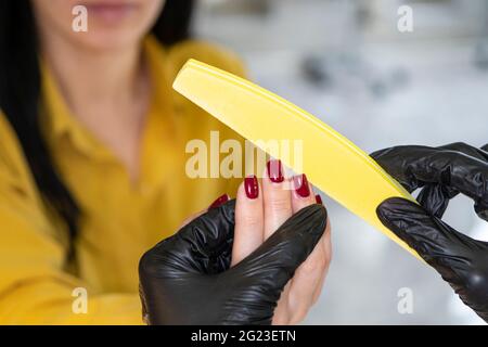 Concetto di industria di bellezza. Donna manicurista master in guanti è lucidare le unghie del cliente utilizzando file. Ritratto di giovane lavoratrice in cosmetologia sal Foto Stock