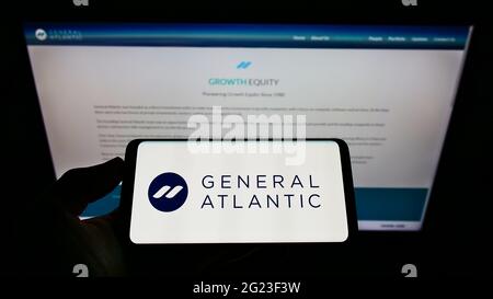 Persona che detiene il cellulare con il logo della società di private equity statunitense General Atlantic sullo schermo di fronte alla pagina web aziendale. Mettere a fuoco il display del telefono. Foto Stock