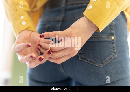 una donna che lotta per rimuovere l'anello di nozze dal dito che tiene le mani dietro la schiena. rimuovere l'anello dal dito. Il concetto di tradimento A. Foto Stock