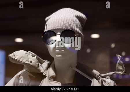 La testa di un manichino in un cappello e occhiali da sole, abbagliamento da vetro e lampade. Manichino in un cappello lavorato a maglia e cappotto da vicino Foto Stock